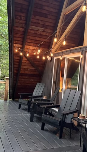 Terraza de una cabaña en forma de A con guirnaldas de luces y sillas Adirondack al anochecer