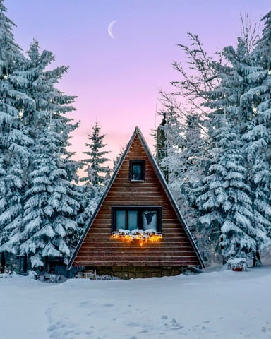 A-frame cabin glowing under a crescent moon surrounded by snow-covered pines