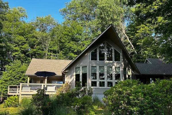 Modern A-frame house with large windows surrounded by dense green forest and landscaping.