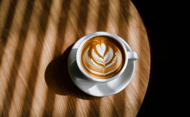 Latte art in a white cup on a wooden table with warm directional light