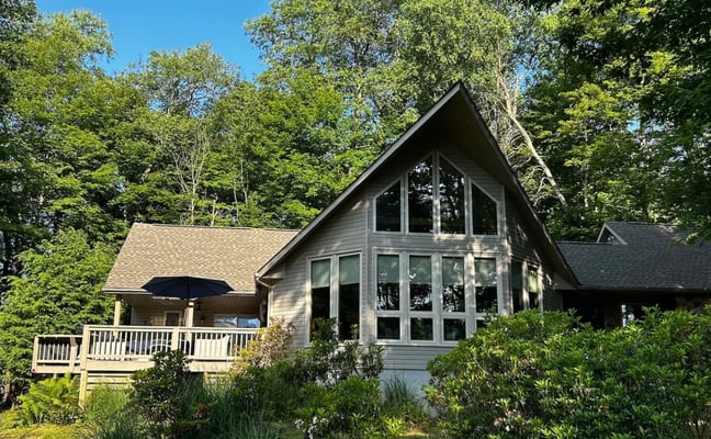 Modern black cabin on stilts surrounded by tall trees at sunset with wraparound deck and large windows